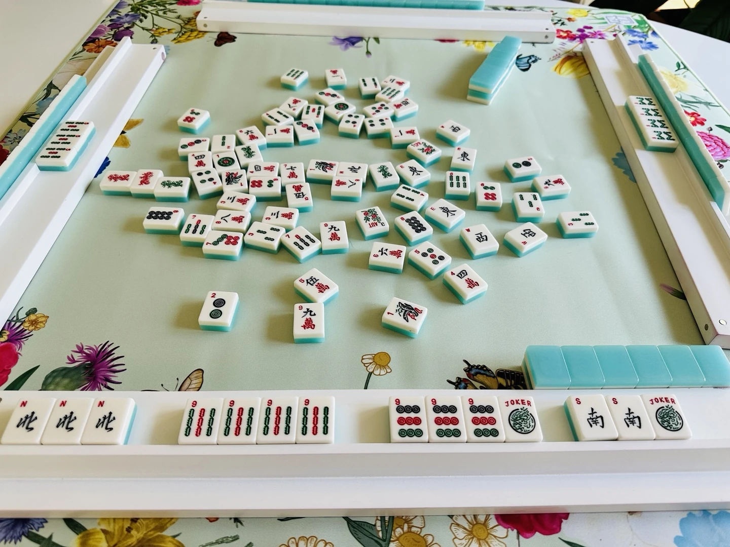 Authentic Mahjong tiles arranged on a floral tabletop with turquoise tile racks